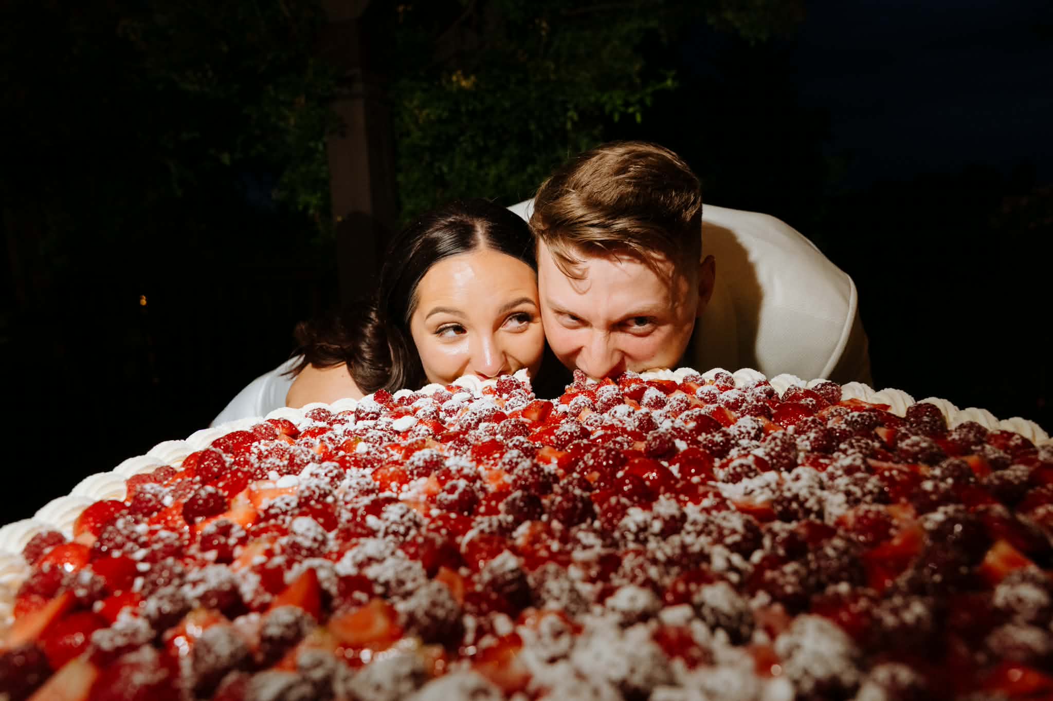 Ola and Mateusz, the founders of e-nvelope, peeking over their strawberry and raspberry wedding cake
